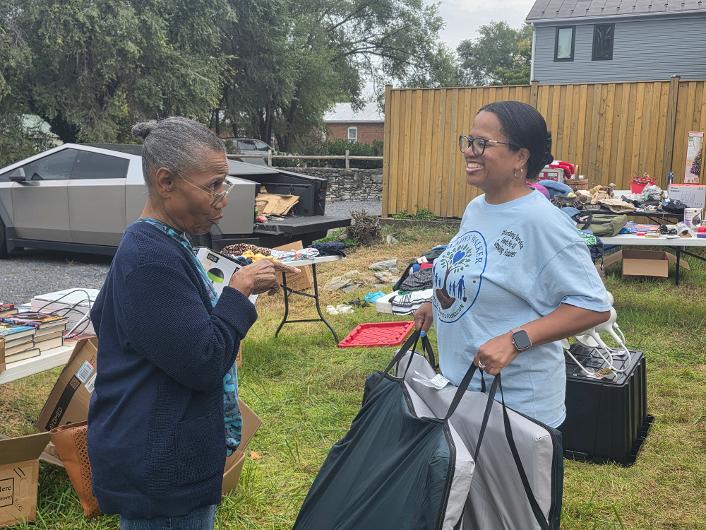 A GWSoSF volunteer smiling and chatting with a shopper among yard sale tables