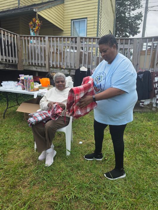 A GWSoSF volunteer showing a plaid item to a seated guest at the yard sale